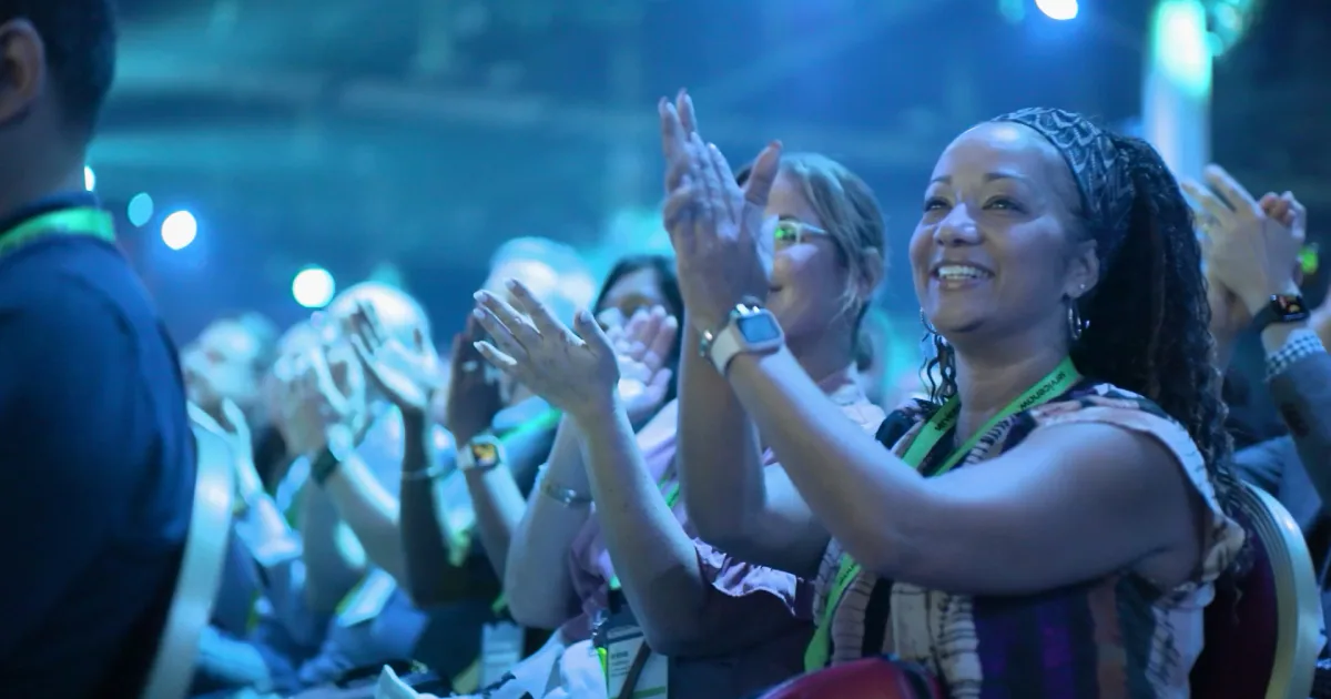 Smiling attendees applauding at ServiceNow Knowledge under blue event lighting